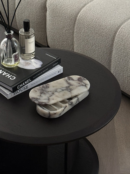 The ourside marble pill box on a dark side table beside a boucle sofa